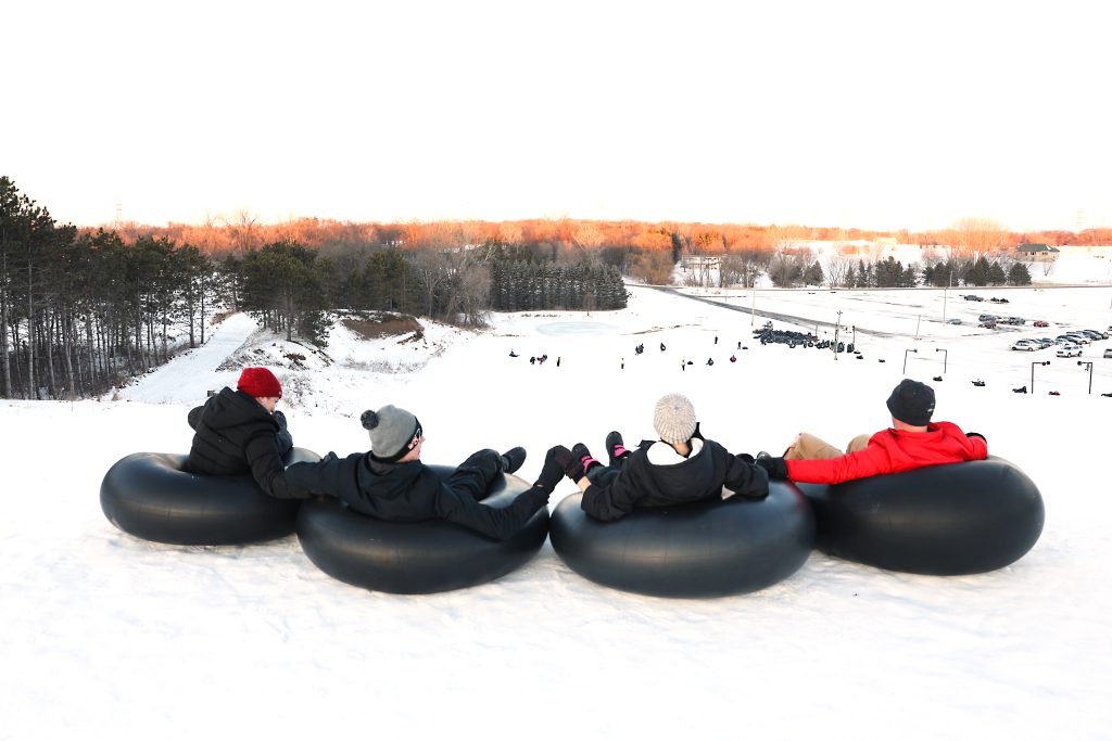 Four snow-tubers enjoying the view on top of the snow hill. 