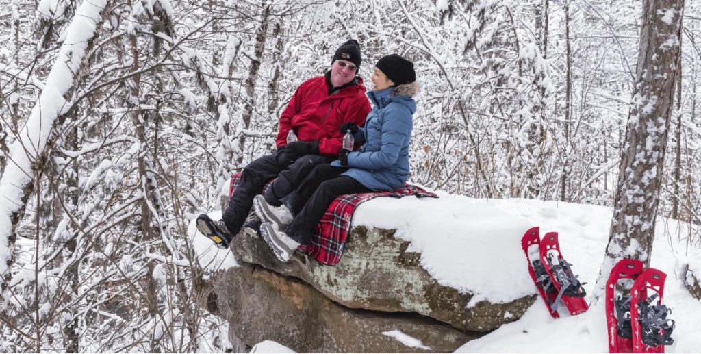Two people sitting on a blanket in the snow after snowshoeing. 