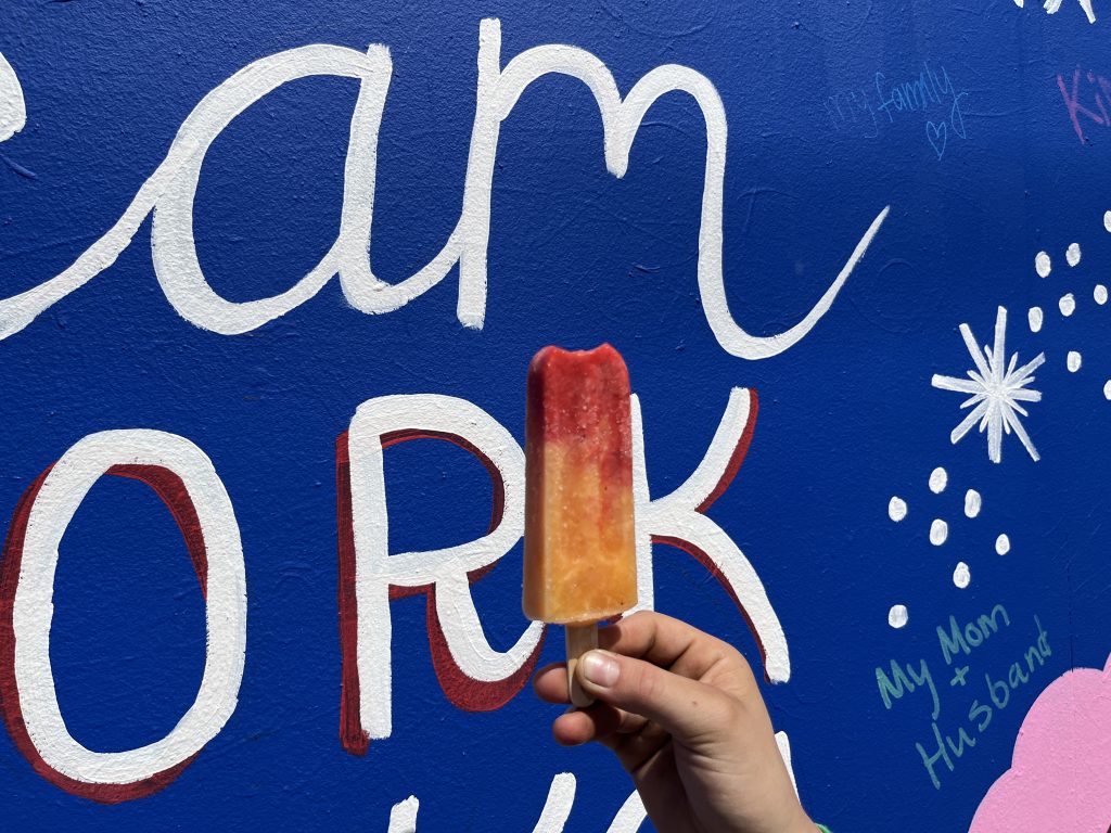 Sticks Popsicle in front of colorful mural