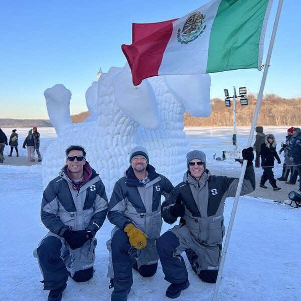 Sculpters with their flag kneel in front of their snow sculpture.