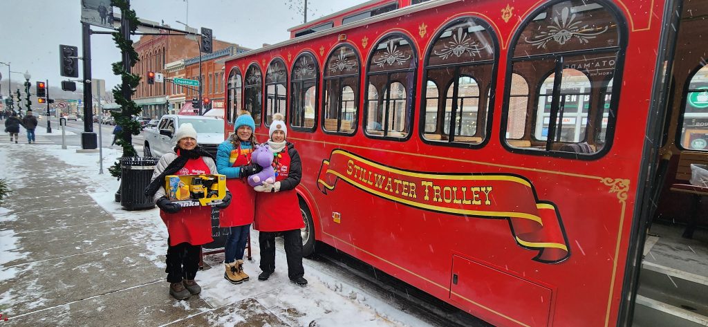 People pose by the Stillwater Trolley with donated toys for kids on a winter day