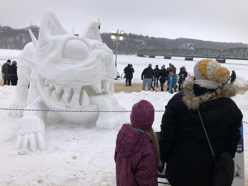 people observing a snow sculpture of a creature